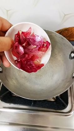 a person holding a bowl with red onions in it on top of a stove burner