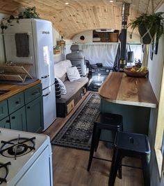 a kitchen and living room in an airstream with wood flooring, white appliances and green cabinets