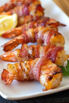 shrimp and bacon skewers on a white plate with lemon wedged garnish