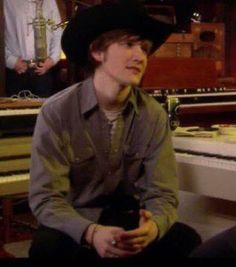 a young man wearing a cowboy hat sits in front of a piano and looks off to the side