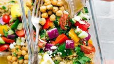 a person is holding a fork over a bowl of food with chickpeas and vegetables