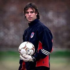 a young man holding a soccer ball in his right hand and looking at the camera