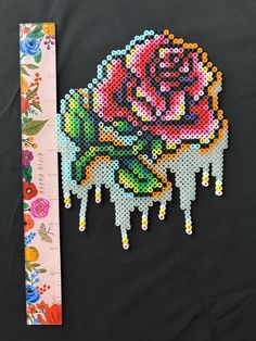 a cross stitch rose next to a ruler on a black background with flowers and leaves