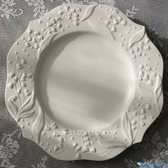 a white plate with ornate designs on the rim and sides is sitting on a lace tablecloth