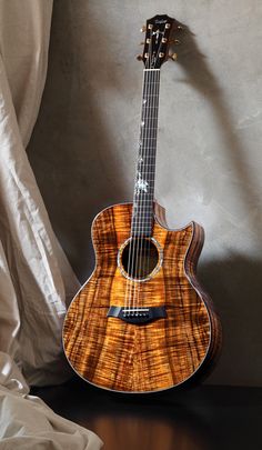 an acoustic guitar sitting on top of a wooden table next to a white cloth covered wall