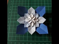 an origami flower is shown on a cutting board with green and blue paper