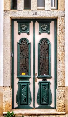 two green doors with decorative designs on the front and side of a white building in europe