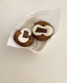 two cookies with white icing and chocolate on top are sitting in a paper wrapper