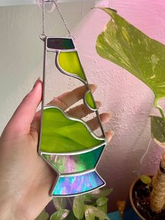 a hand holding a stained glass vase in front of a houseplant and potted plant