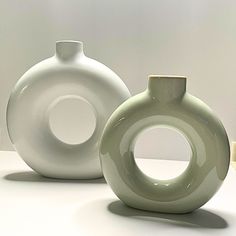 two white vases sitting next to each other on top of a table with one in the middle