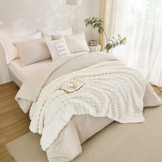 a bed with white comforters and pillows in a room next to a window,