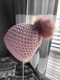 a knitted hat with a pink pom - pom sits on top of a mannequin