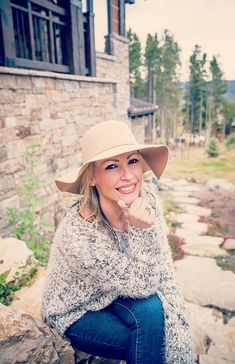 a woman in a hat is sitting on some rocks and posing for the camera with her hand under her chin