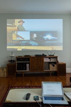 a laptop computer sitting on top of a wooden table in front of a projector screen