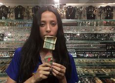 a woman holding money in front of her face and looking at the camera while standing next to a rack of necklaces