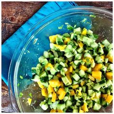 a glass bowl filled with cucumbers and other vegetables on top of a wooden table