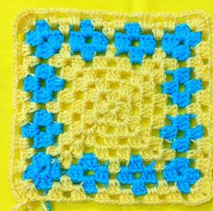 a crocheted square with blue and yellow squares on it, sitting on a yellow surface