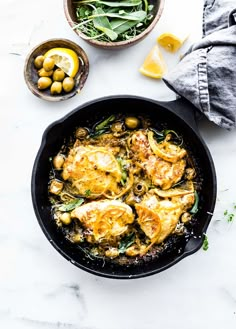 a skillet filled with chicken, olives and spinach on top of a white table