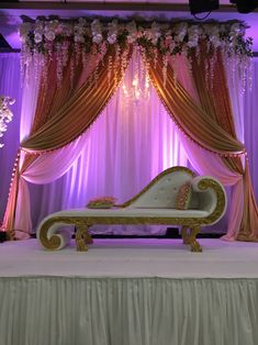 a white couch sitting on top of a table under a purple and gold drape