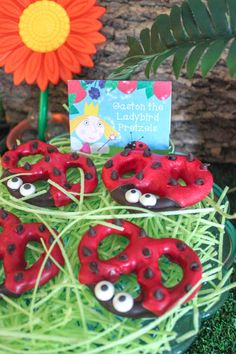 there are some red donuts with googly eyes in the grass next to a flower