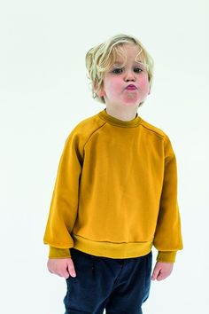 a young boy standing in front of a white background wearing a yellow sweatshirt and blue pants