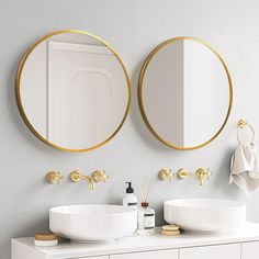 two round mirrors on the wall above sinks in a white bathroom with gold trimmings