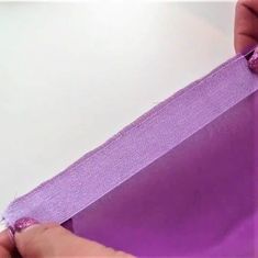 someone is cutting the edge of a piece of purple fabric with scissors and tape on it