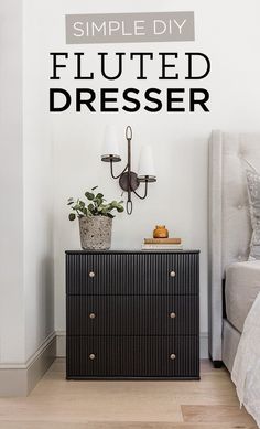 a bedroom with a black dresser next to a white bed and a plant on top of it