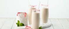 three glasses of milkshake with candy canes and peppermint on the side