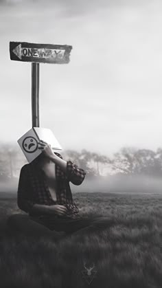 a man sitting in the grass with a paper hat on his head and a street sign above his head