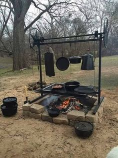 an outdoor cooking area with pots and pans on the fire pit in the middle