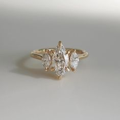 a three stone diamond ring sitting on top of a white surface with the center setting in yellow gold