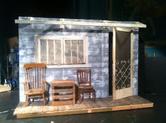 a doll house with two chairs and a table in front of the door, on a stage