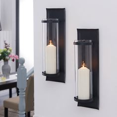 two black wall sconces with white candles on them in front of a dining room table