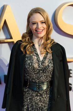 a woman standing in front of a sign wearing a black jacket and dress with lace on it