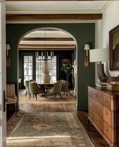 an archway leads into a formal dining room with green walls and wood trimmings