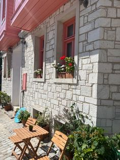 two wooden tables and chairs sitting in front of a brick building with red shutters