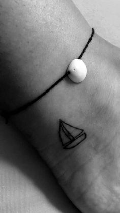 a black and white photo of a person's foot with a small sailboat tattoo on it