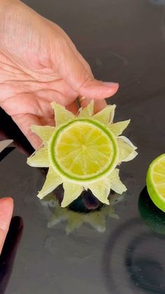 a person holding a cut up lime on top of a black table with other pieces