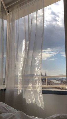 an open window with sheer curtains in front of a cityscape and the sky