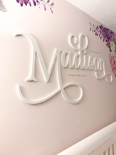 the name madison written in cursive white on a pink wall with purple flowers