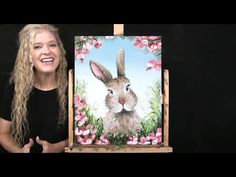 a woman standing next to an easel with a painting on it's side