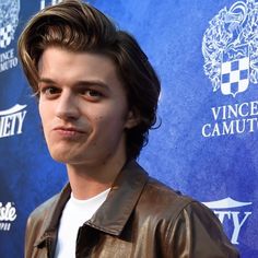 a young man in a brown leather jacket posing for the camera on a red carpet