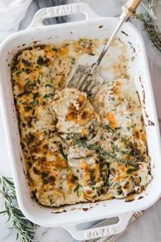 a white casserole dish with chicken and cheese in it, garnished with fresh herbs