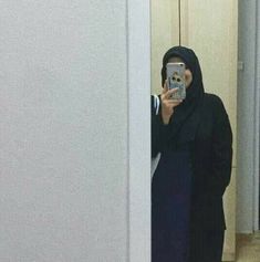 a woman taking a selfie in front of a mirror with her cell phone and wearing a black hijab