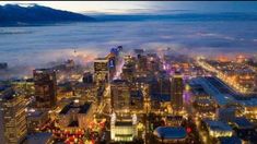 an aerial view of a city at night with fog in the air and mountains in the distance