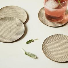 three coasters with leaves on them sitting next to a glass filled with water and ice