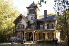 an old house with people standing in front of it and cars parked on the driveway