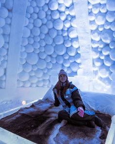 a woman sitting on top of a bed in an ice hotel with balls all over the walls