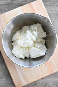 a metal bowl filled with mashed potatoes on top of a wooden cutting board next to a knife